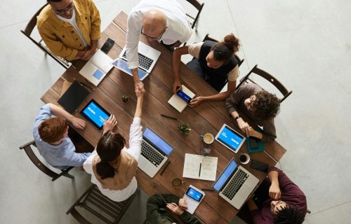 Top view of a diverse team collaborating in an office setting with laptops and tablets, promoting cooperation.